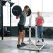 Muscular young man training in gym squatting with barbell working out with coach attractive girl wearing sports clothing. People, workout and leisure concept.
